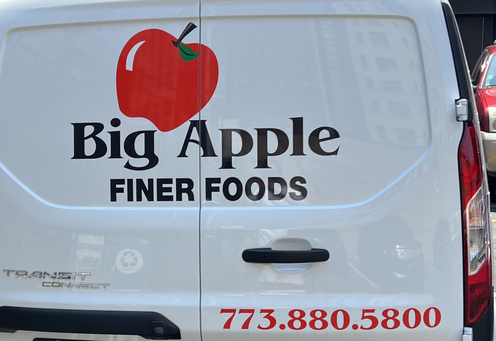The back of a white Big Apple Finer Foods delivery van, with the red apple logo and the store phone number